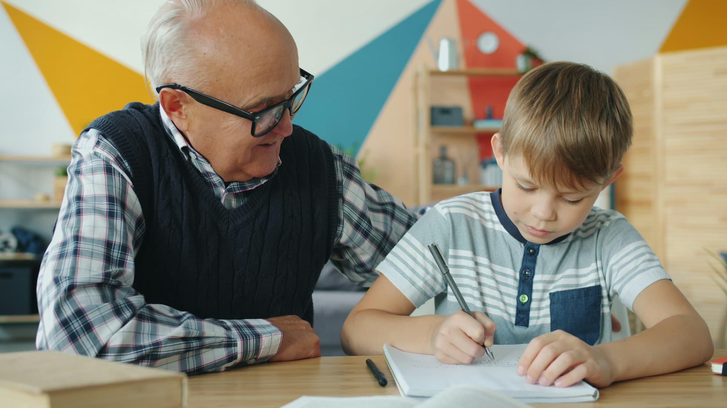 An older man and a young boy writing together at a table