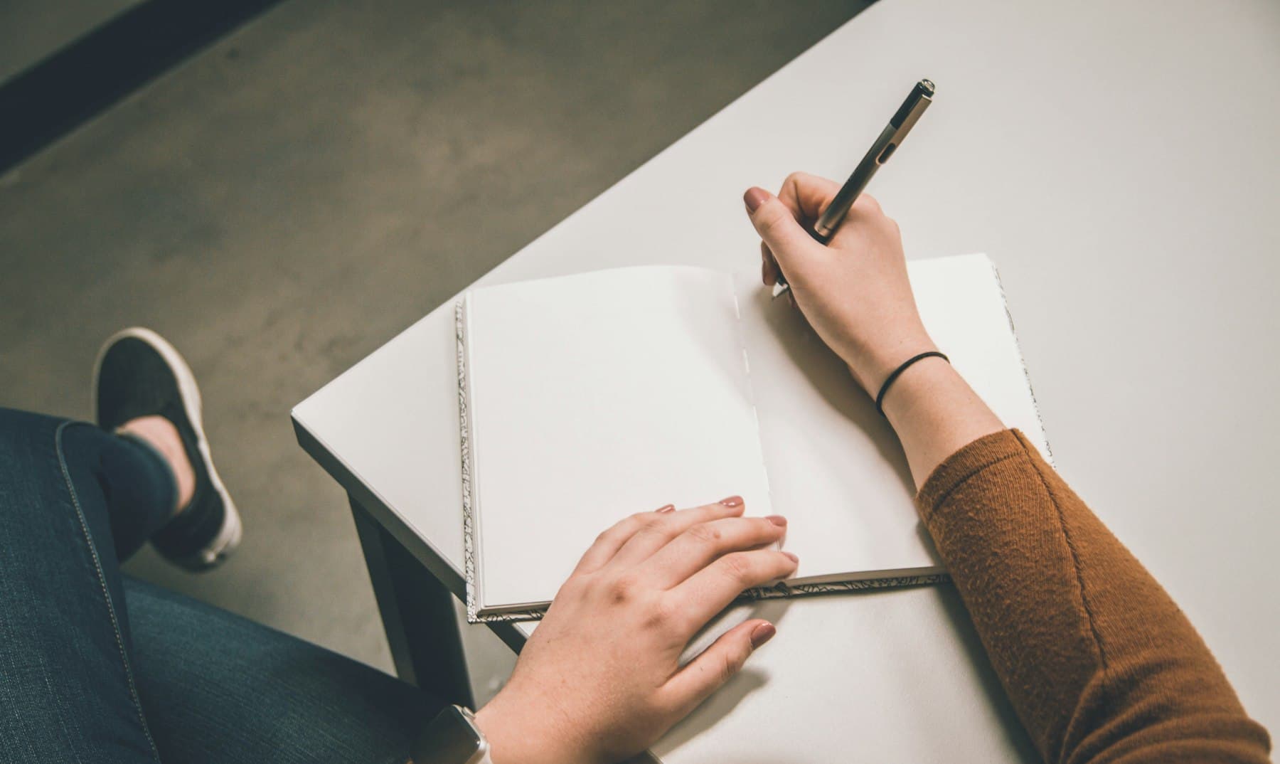 A person writing in an open notebook at a desk, seen from above