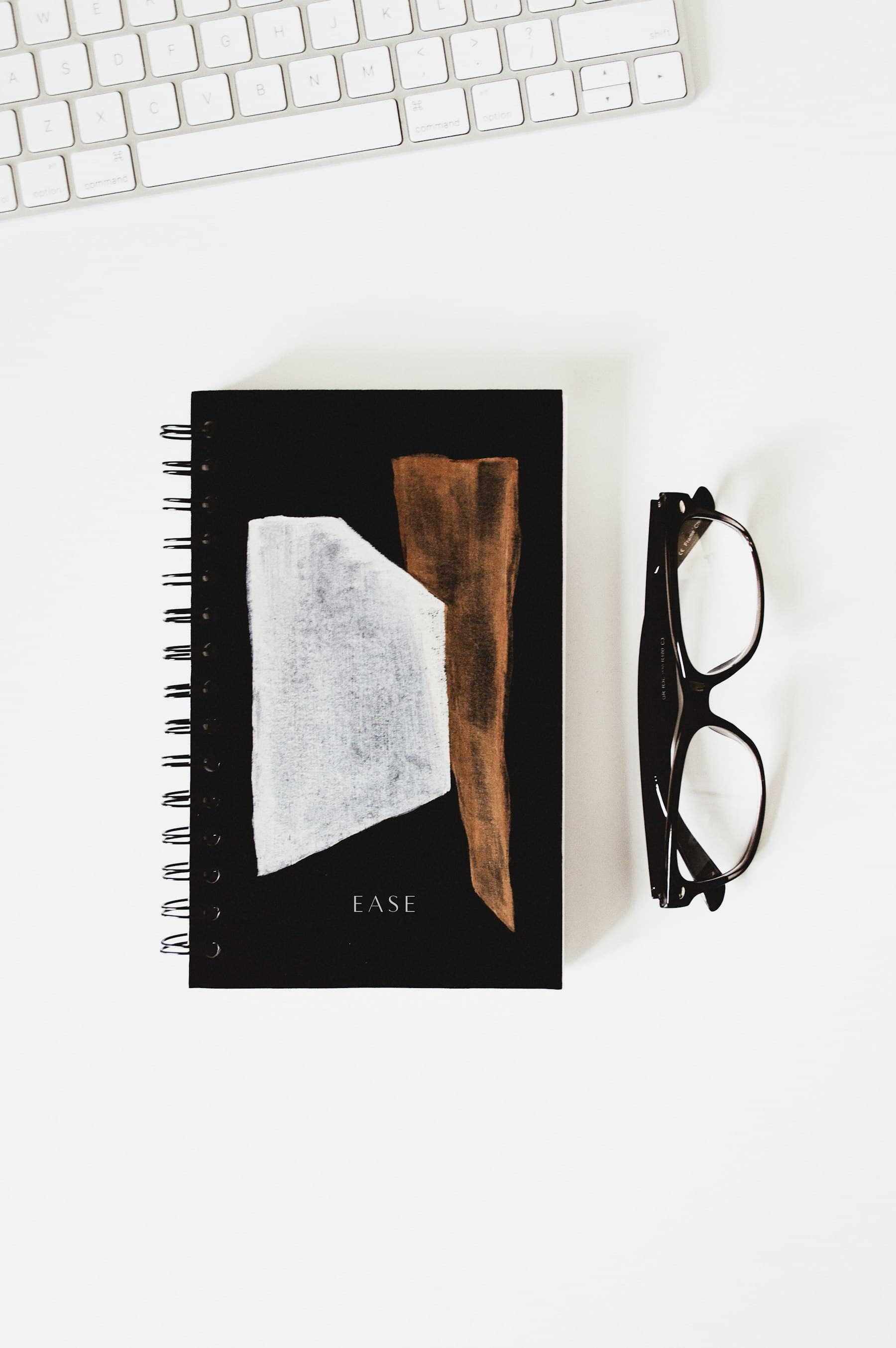 A black notebook and reading glasses arranged on a white desk