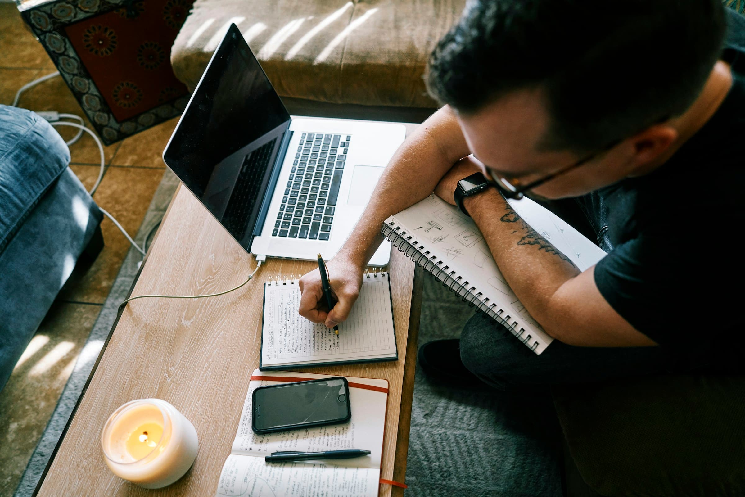 A student writing notes at a desk beside an open laptop